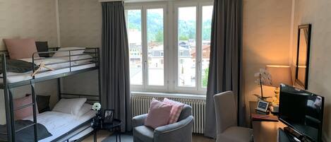 Una habitación con literas, un escritorio con computadora, una silla, un radiador y una ventana con cortinas.