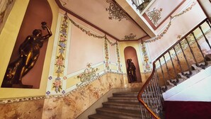 Eine prächtige Treppe mit aufwendiger Geländerarbeit und dekorativen Verzierungen, die zu einer oberen Ebene mit einem Balkon führt.