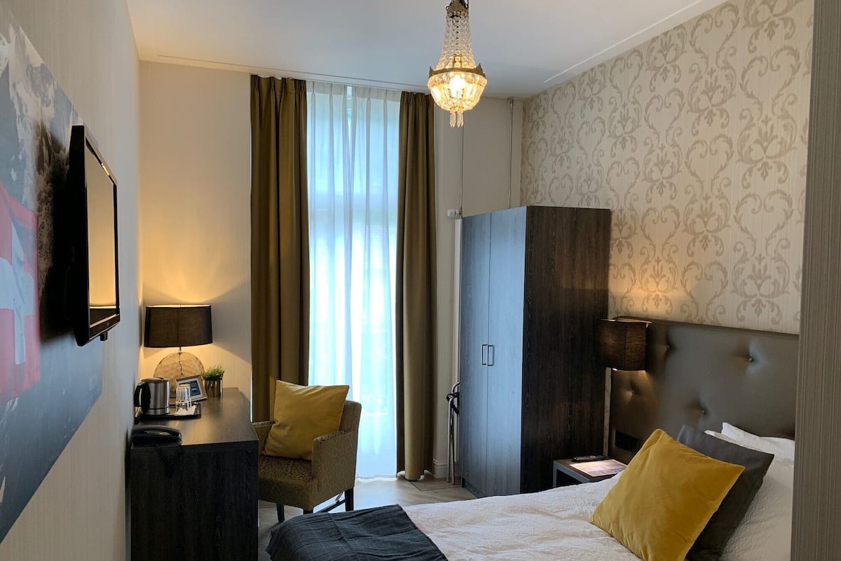 Une chambre d’hôtel comprenant un lit, un bureau, une chaise, une armoire et un lustre.