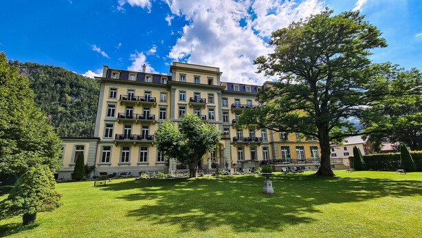 Ein mehrstöckiges Hotel mit einer symmetrischen Fassade, Balkonen und einem gepflegten Rasen.