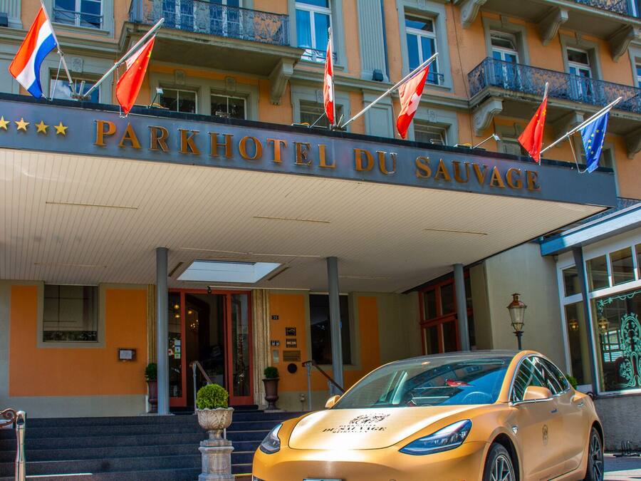 La entrada del Parkhotel du Savorgnan con un coche dorado estacionado en frente.