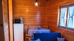 A cozy cabin interior with a blue sofa, a small table with checkered tablecloth, a microwave, and a refrigerator.