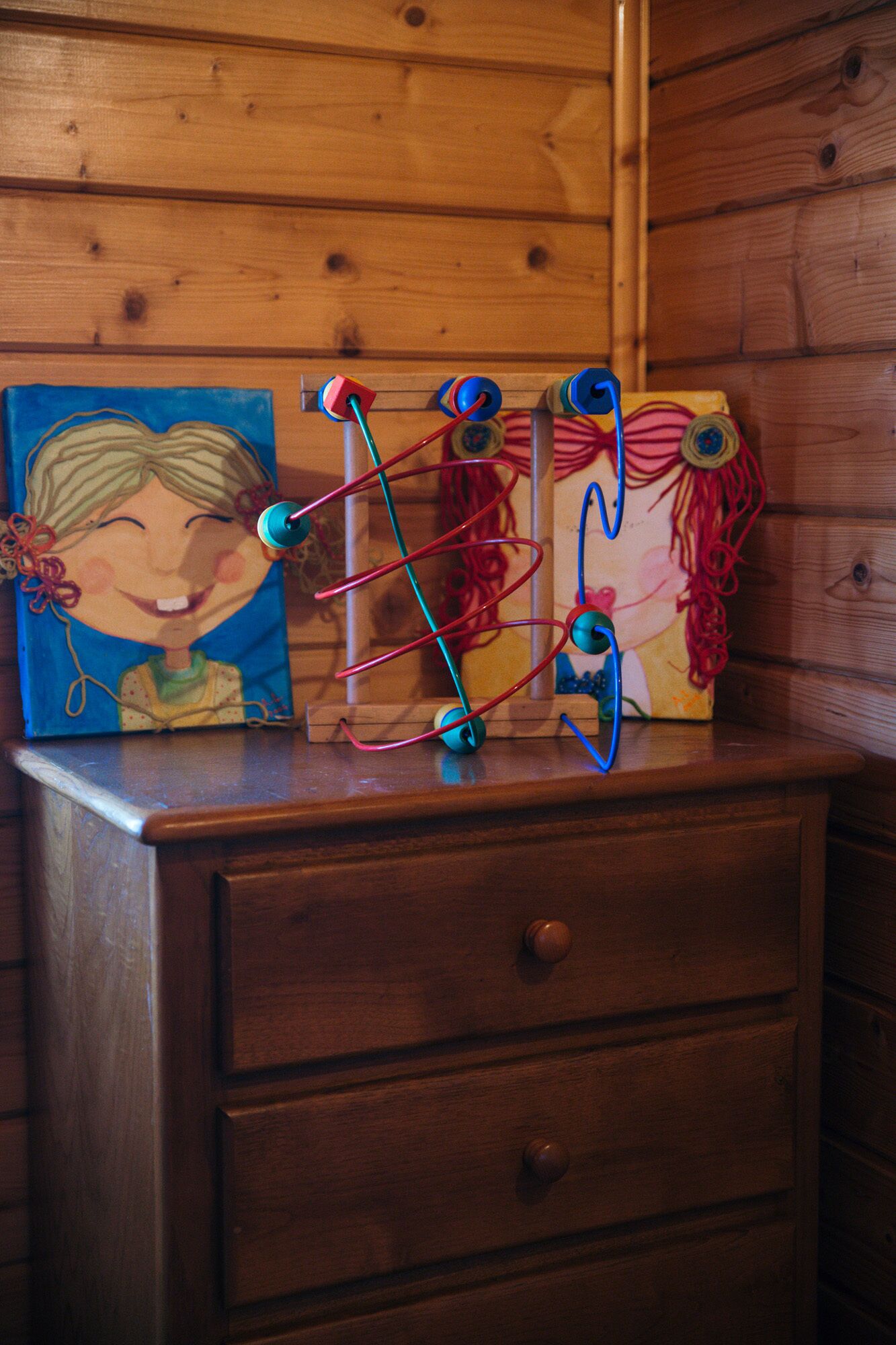 Une commode en bois ornée d’un tableau représentant une femme et d’un appareil mécanique avec des fils de couleurs vives.