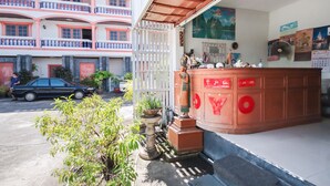 A building with a red and white facade, a balcony with pink railings, and a small garden area with potted plants. - OYO 1172 Goodnight Resort (Phuket)