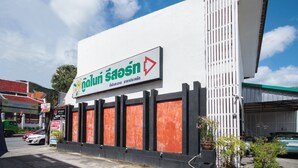 A building with a sign that reads "Nalu Saosin" and a large white wall with vertical black panels. - OYO 1172 Goodnight Resort (Phuket)