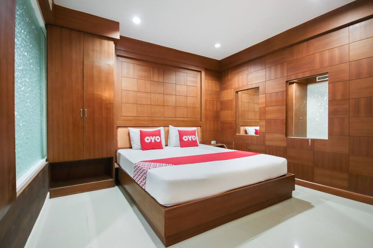 A modern bedroom with a large bed, wooden paneling on the walls, and a window with a view.