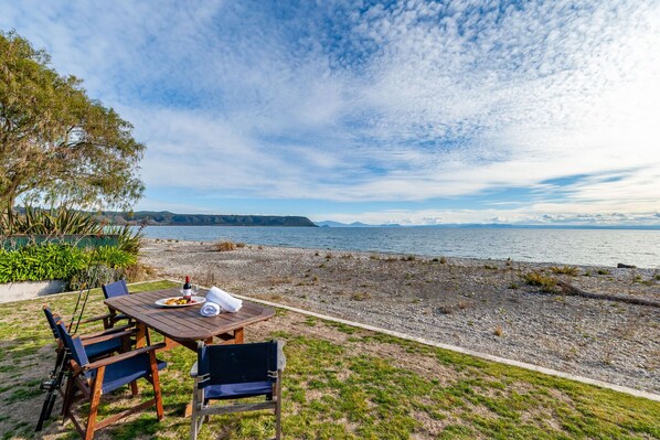An outdoor dining area with a table and chairs, a bottle of wine, and a glass of water. - Waitahanui Lakefront Escape - Waitahanui Home (Waitahanui)