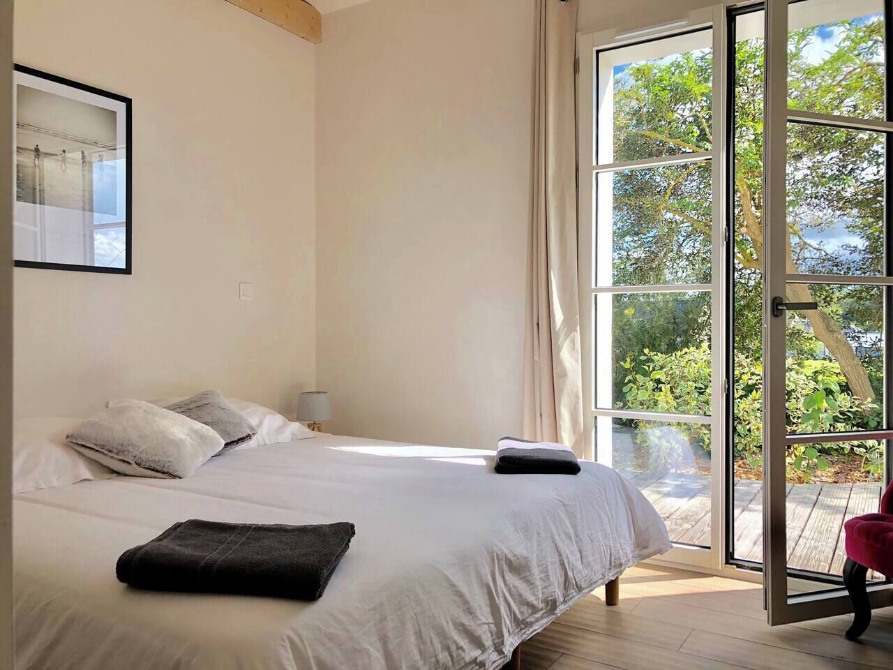 Une chambre avec un grand lit, une fenêtre donnant sur un paysage verdoyant et un fauteuil rouge.