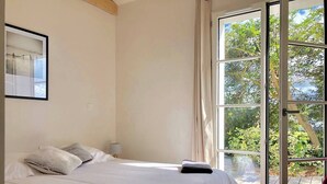 Un dormitorio con una cama grande, una ventana que da a zonas verdes y una silla roja.