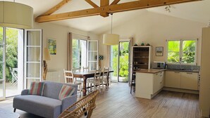 Un amplio espacio habitable con sofá, mesa de comedor y sillas, una cocina con microondas, y ventanas grandes que ofrecen vistas a zonas verdes.
