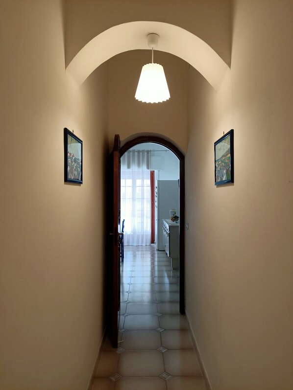 A hallway with a tiled floor, a ceiling light, and two framed pictures on the walls.