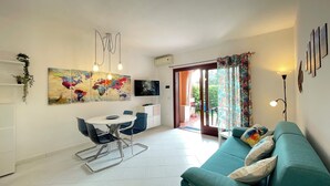 A modern living room with a teal sofa, a dining area with a white table and chairs, and a large abstract painting on the wall.