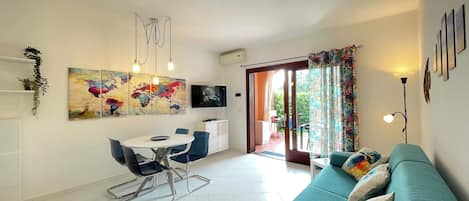 A modern living room with a teal sofa, a dining area with a white table and chairs, and a large abstract painting on the wall.
