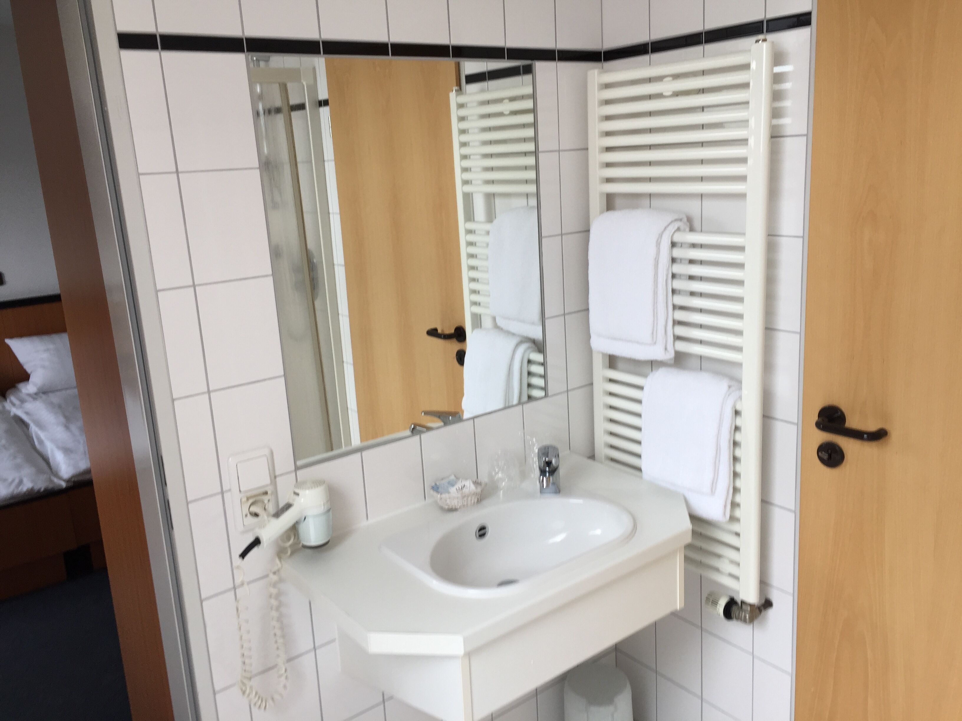 A bathroom with a white sink, mirror, towel rack, and a wooden door.