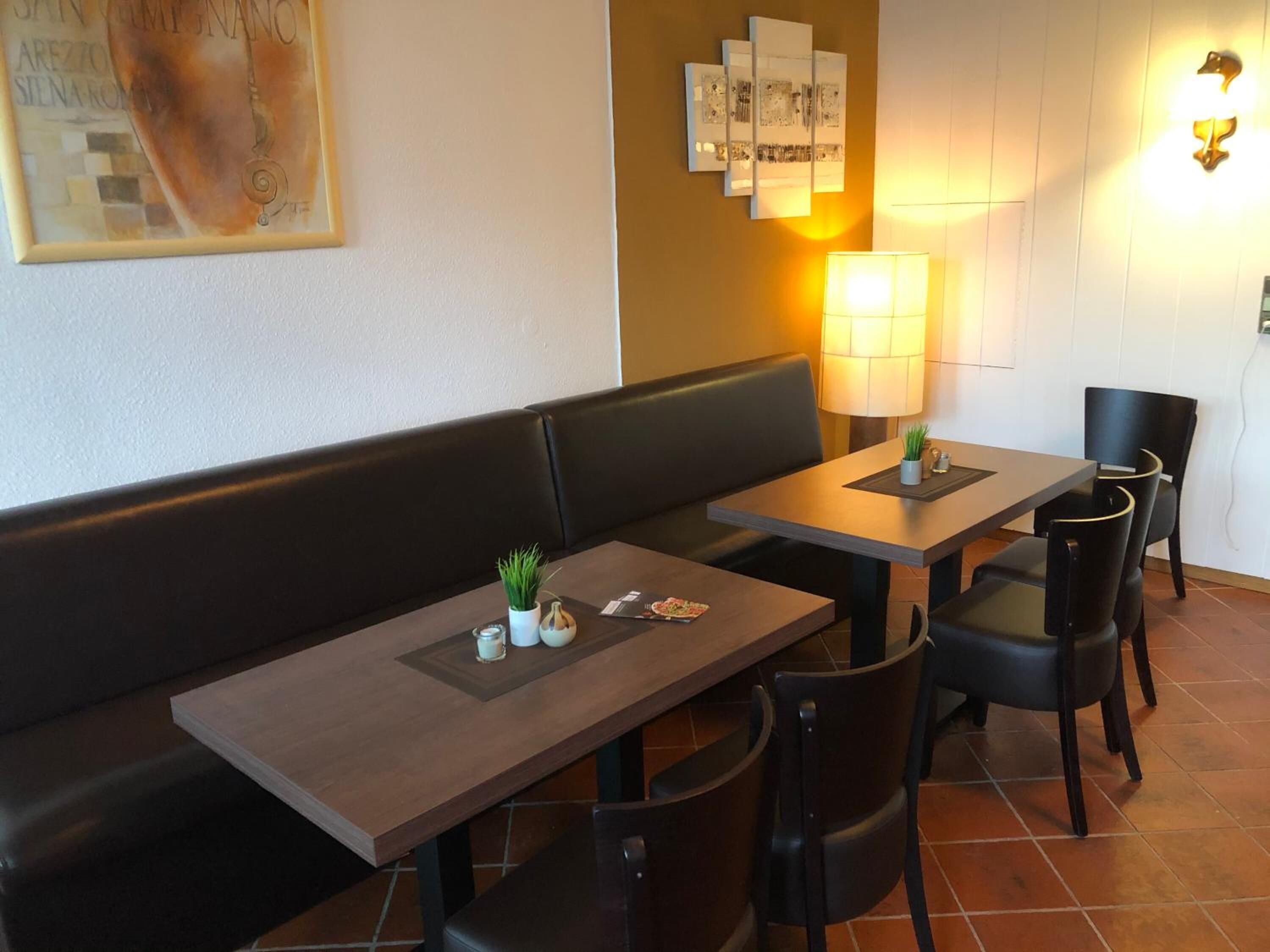 A restaurant with a long wooden bench, two tables with chairs, and wall-mounted artwork.