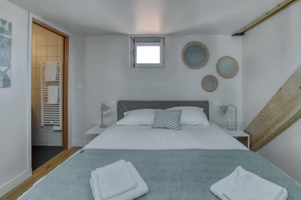 A bedroom with a bed, bedside tables, a window, and a wooden slanted ceiling.