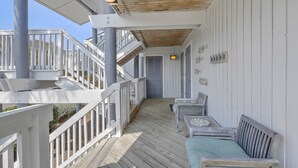 Une terrasse en bois couverte, dotée de rampes blanches, d’un escalier et d’un espace salon extérieur.