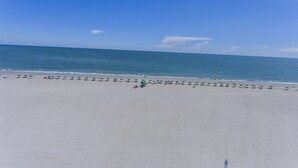 Une vaste plage bordée de rangées de parasols, offrant une vue dégagée sur l’océan.