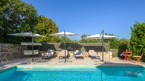 Zona de piscina con sillones, sombrillas y un muro de piedra.