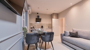 Ein modernes Wohnzimmer mit einem grauen Sofa, einem Esstisch für vier Personen und einer Küche im Hintergrund.