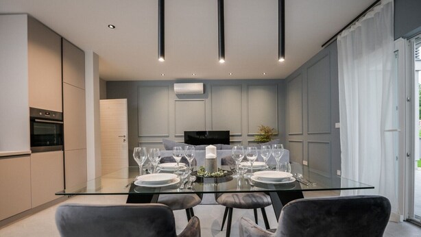 A modern dining area with a glass table, grey upholstered chairs, and a flat-screen TV in the background. - Modern apartment Lacrima 2 in villa with a pool on Krk (Silo)