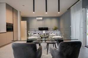 Un comedor moderno con una mesa de vidrio, sillas grises tapizadas y un televisor de pantalla plana al fondo.