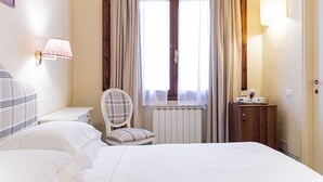 A hotel room with a bed, a chair, a small table, a lamp, and a window with curtains. - Casa Uffizi Tower House Boutique Hotel (Florence)
