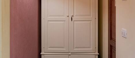 A narrow hallway with a white wardrobe, a wall-mounted light, and a door on the right.