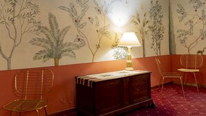 A room with a mural of trees and plants on the wall, a wooden cabinet, two wireframe chairs, and a table with a lamp. - Casa Uffizi Tower House Boutique Hotel (Florence)