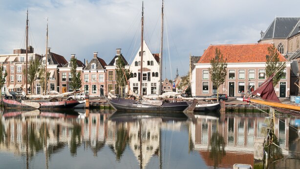 A canal with boats docked, surrounded by traditional buildings with red roofs and white facades.