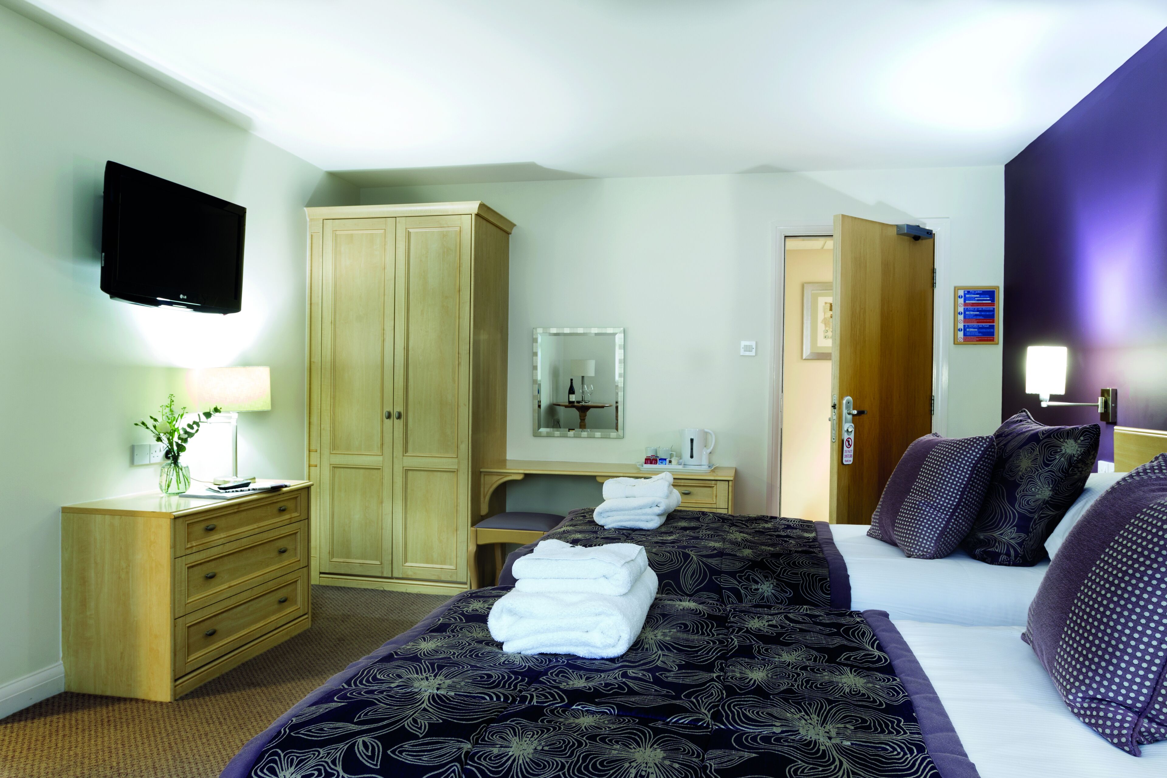 Habitación de hotel con una cama grande, un armario, un escritorio con silla, un televisor y la puerta del baño.