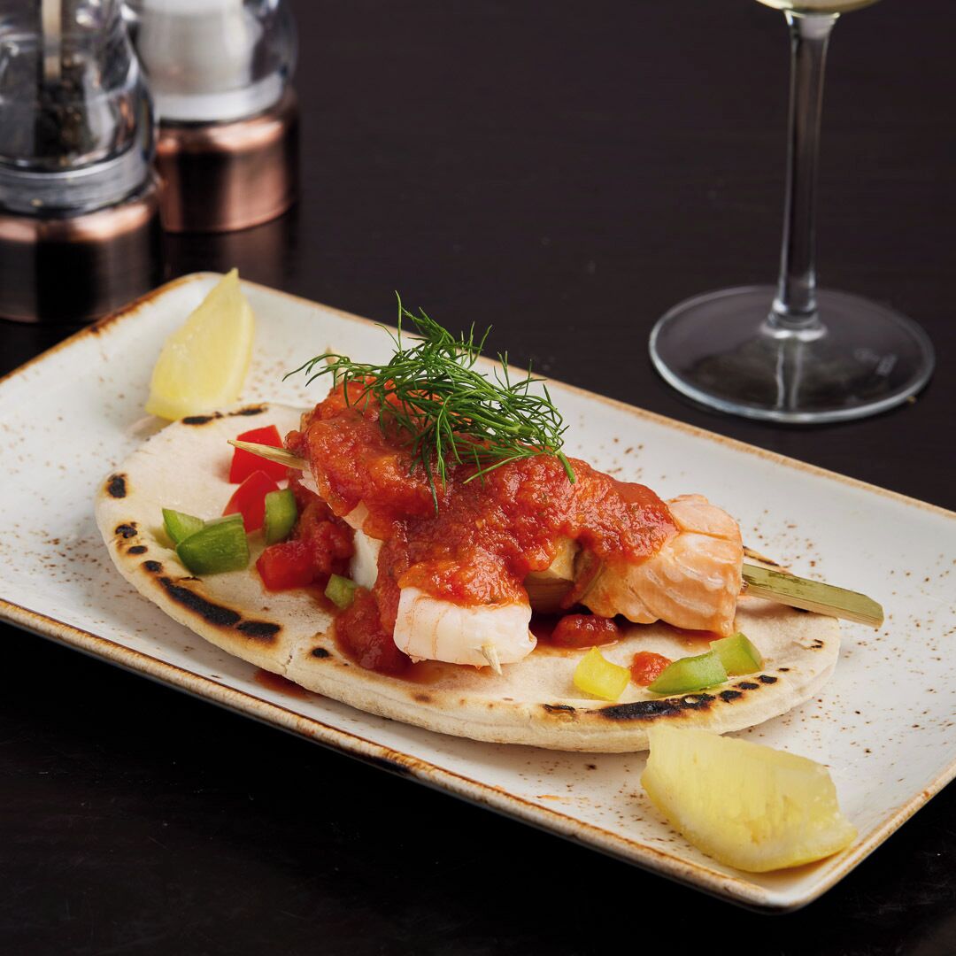 Une assiette contenant un taco au poisson, garni d’aneth et de légumes coupés en dés, sur une assiette en céramique.