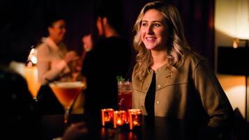 A dimly lit bar area with a person seated at a table, a cocktail glass, and candles on the table.