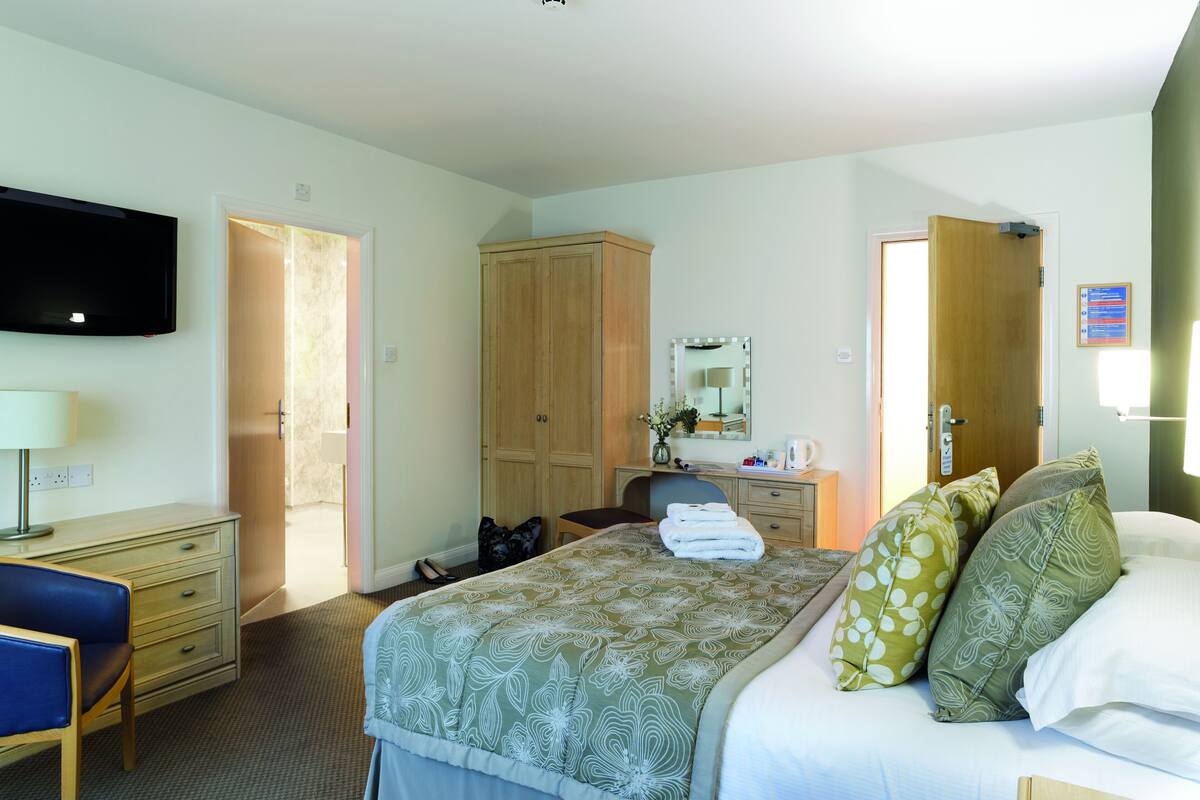 Une chambre d’hôtel équipée d’un lit, d’un bureau, d’une chaise, d’une armoire, d’une télévision et d’une porte de salle de bain.
