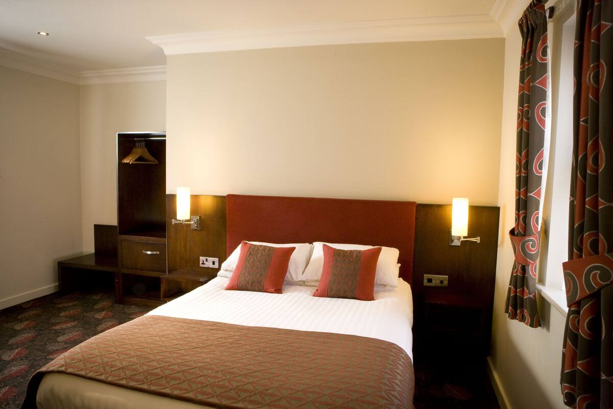 Une chambre d’hôtel avec un grand lit, deux tables de chevet, une armoire et un miroir.