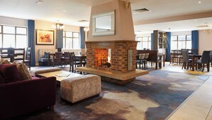 A spacious lobby with a central stone fireplace, comfortable seating, and large windows. - Burntwood Court Hotel (Barnsley)