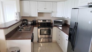 A kitchen with white cabinets, stainless steel appliances, a sink, and a trash can. - Luxurious Apartment with  Wi-Fi and Private Bathroom (Fort McMurray)