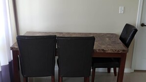 A dining table with four chairs, a door, and a light switch on the wall. - Luxurious Apartment with  Wi-Fi and Private Bathroom (Fort McMurray)