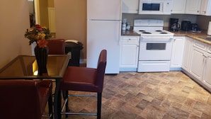 Cocina compacta con armarios blancos, un refrigerador, estufa y microondas. Hay una mesa de comedor con sillas y un florero con flores.