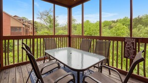 A covered outdoor area with a table and chairs, a ceiling fan, and a view of greenery and buildings. - Rustic-Chic 4BR + Loft Cabin | Golf & Show Discounts! (Branson)
