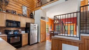 A spacious kitchen with wooden cabinets, a stainless steel refrigerator, and a black stove. - Rustic-Chic 4BR + Loft Cabin | Golf & Show Discounts! (Branson)