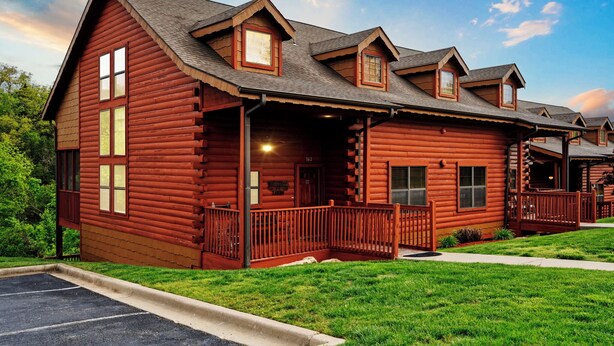 A log cabin-style hotel with a porch, multiple windows, and a parking lot. - Rustic-Chic 4BR + Loft Cabin | Golf & Show Discounts! (Branson)