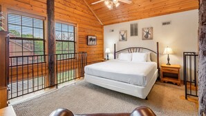A wooden cabin bedroom with a bed, two bedside tables, a ceiling fan, and a view of the outside. - Rustic-Chic 4BR + Loft Cabin | Golf & Show Discounts! (Branson)