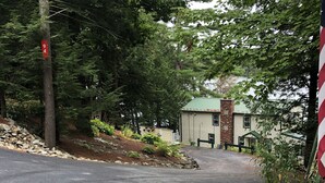 A paved driveway leading to a building with a green roof, surrounded by trees and a stone wall.