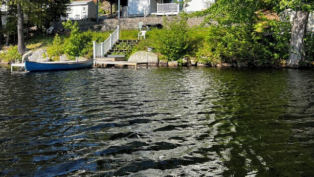 A lakeside property with a dock, a boat, and a house with a balcony overlooking the water.