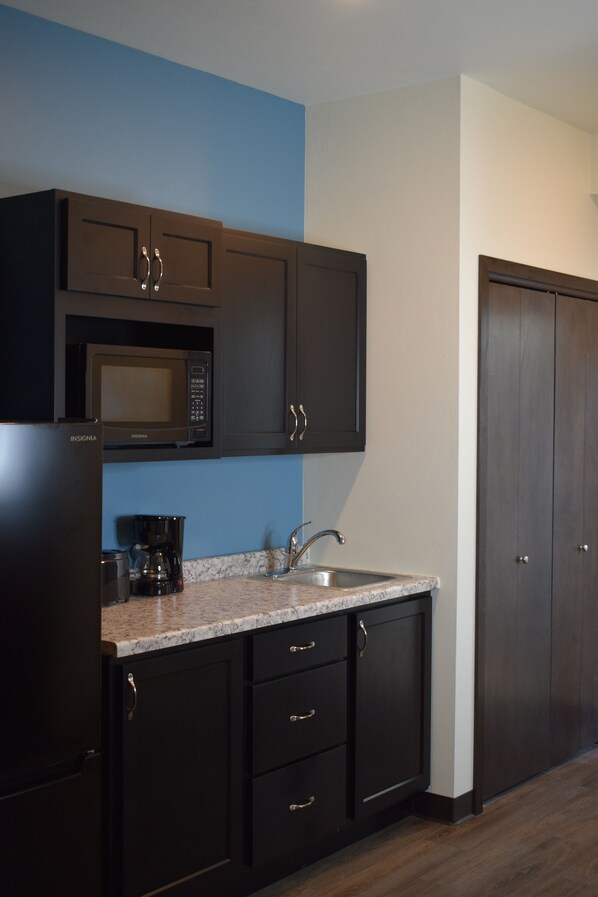 Una cocina moderna con gabinetes oscuros, microondas integrado, cafetera y un lavabo.