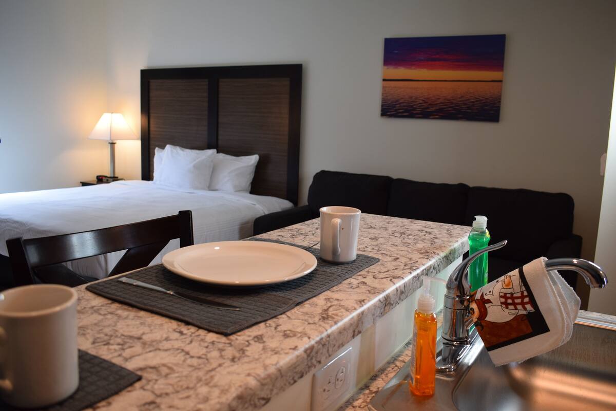 A hotel room with a bed, a sitting area with a couch, a dining table with a plate, a mug, and a bottle of soap.
