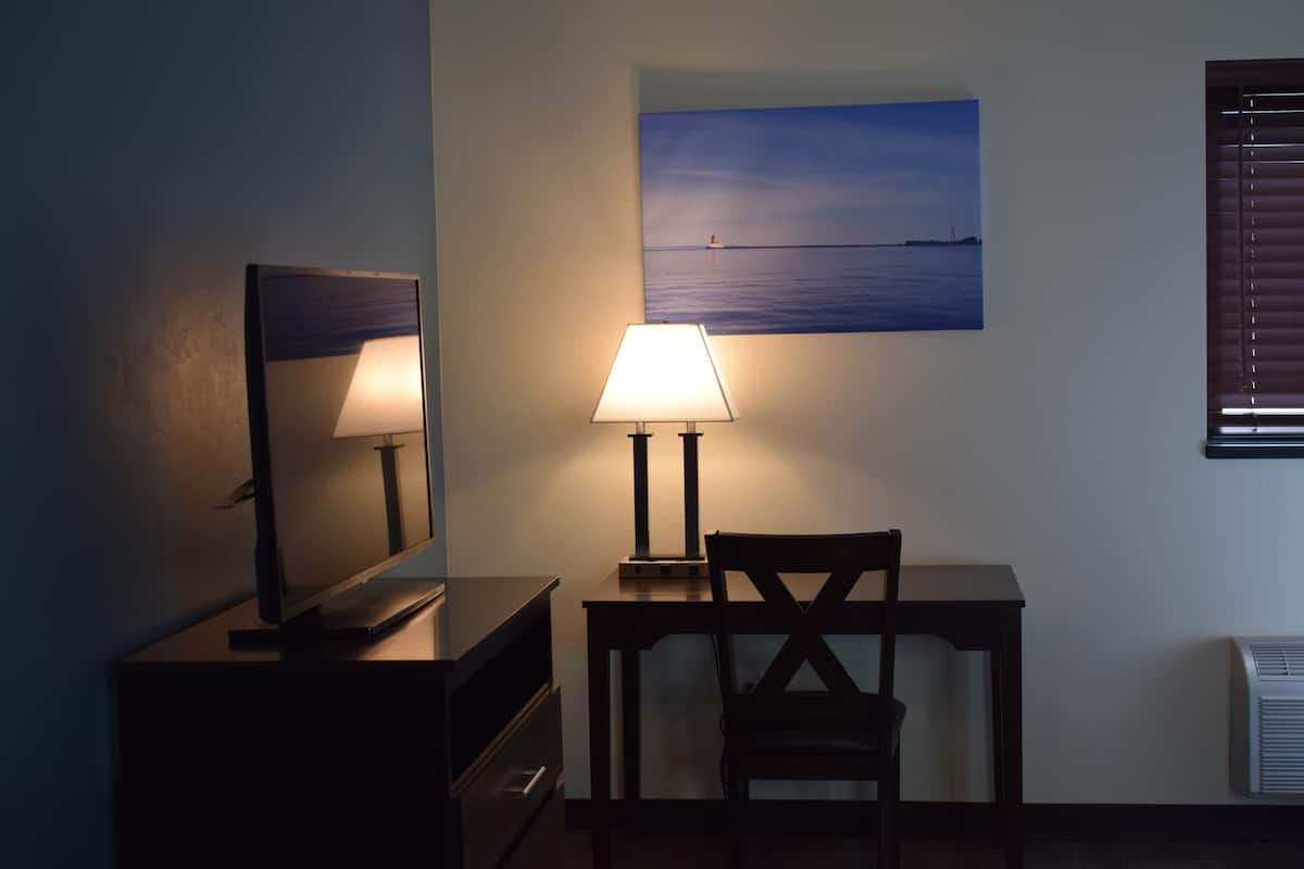 A room with a desk, chair, lamp, mirror, and a painting of a seascape.