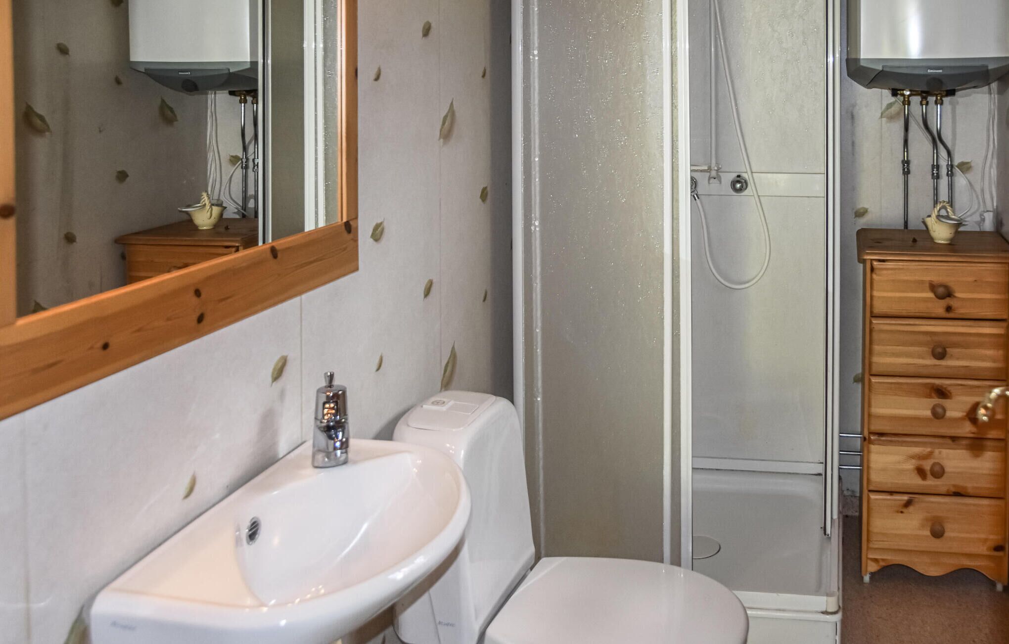Un baño con lavamanos blanco, inodoro, ducha y armarios de madera.