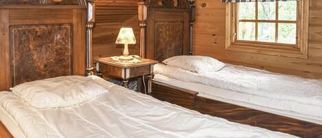 Habitación de cabaña de madera con dos camas, una mesita de noche con lámpara y ventana con cortina a cuadros.